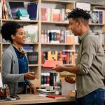 A young black female librarian helping a young black man in a library